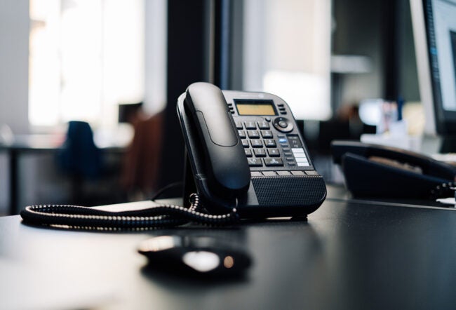 A black office telephone with a cord is on a desk, representing communication in a professional workspace.