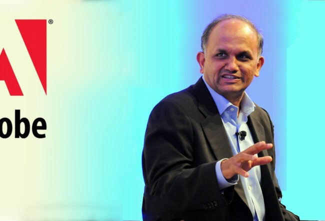 A person in a suit, speaking and gesturing, stands near the Adobe logo.