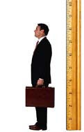 A person in a suit holding a briefcase stands next to an oversized ruler, highlighting height comparison or measurement.