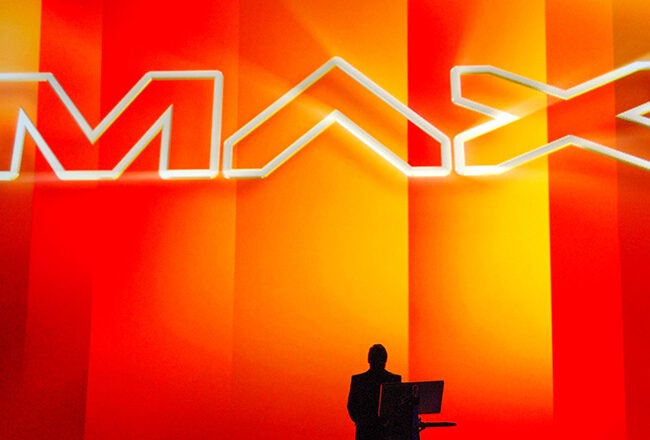Silhouette of a person standing at a podium with the word "MAX" in large, bold letters on a vibrant red and orange background.