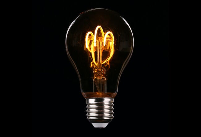 A lit incandescent light bulb with glowing filament against a black background, representing ideas or innovation.