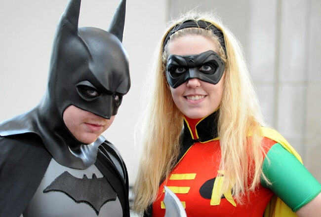 Two people are dressed as Batman and Robin in cosplay costumes, with detailed masks and outfits representing the iconic superhero duo.