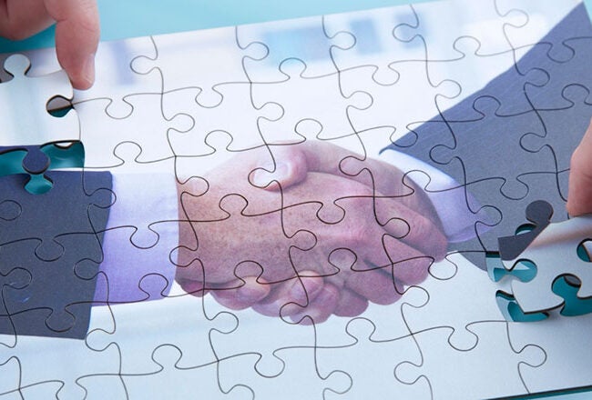 A puzzle showing an image of a handshake being assembled, symbolizing partnership or cooperation. Two hands are placing the final pieces.