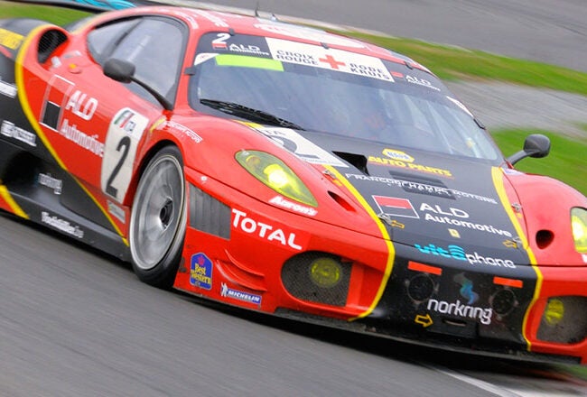 Red and yellow race car with the number 2, speeding on a track. The car is covered in various sponsor logos and decals.
