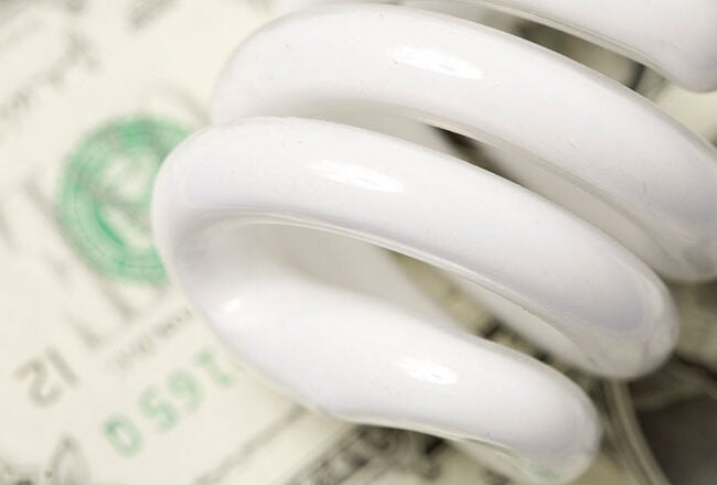 A coiled energy-efficient light bulb lying on U.S. dollar bills, representing the concept of energy cost savings or eco-friendly investments.