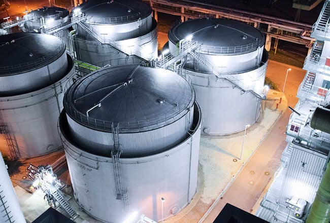 Overhead view of an industrial facility at night, featuring several large cylindrical storage tanks and illuminated equipment.