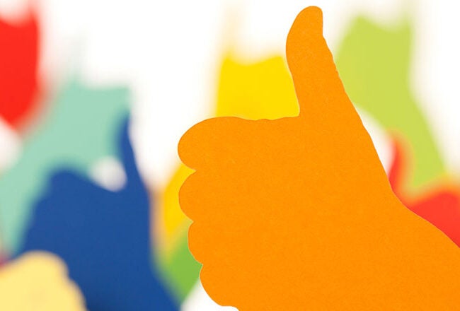 A colorful paper cut-out illustration of a hand giving a thumbs up, with a blurred background of more multicolored thumbs-up shapes.