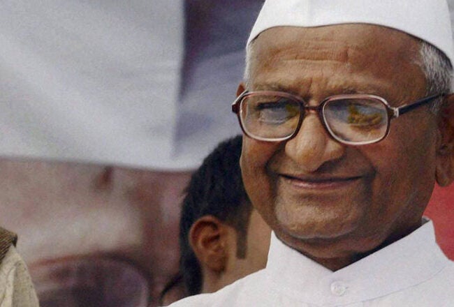 A person wearing glasses and a white cap raises a clenched fist, smiling confidently.