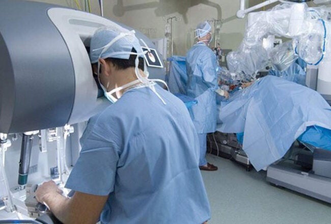 The image shows a surgical room with a robotic surgery system in use. Medical professionals in scrubs and masks are operating a da Vinci Surgical System, which assists in precision surgeries.