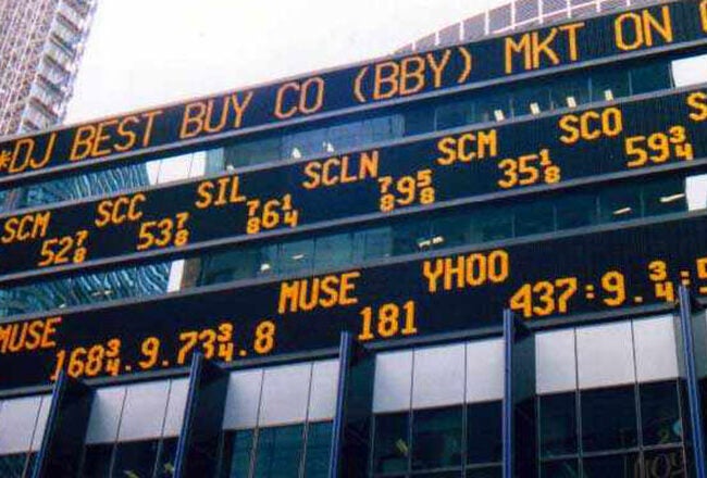 An electronic stock ticker display showing various stock symbols and prices situated on the exterior of a building.