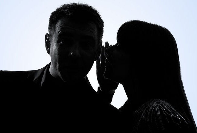 Silhouette of two people, one whispering to the other, against a light background, suggesting secrecy or sharing a secret.