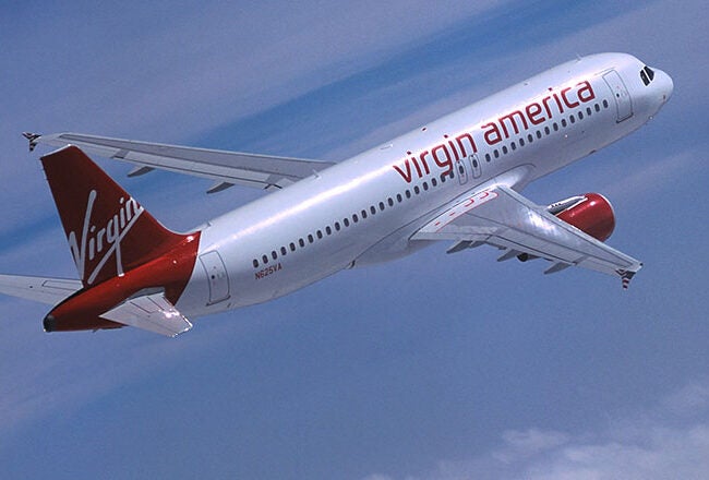 A Virgin America airplane flying in the sky, featuring the airline''s red and white branding.