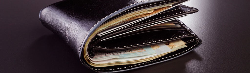 A black leather wallet bulging with banknotes, placed on a dark surface.