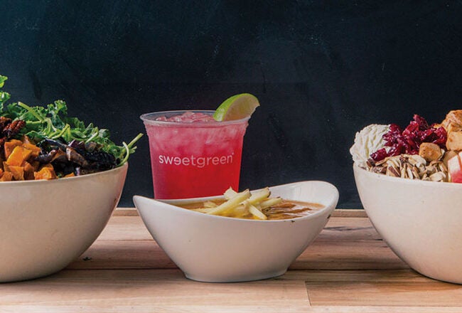 Three bowls with fresh salads, a reddish drink with lime, and a small bowl of fries on a wooden surface.