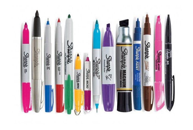 Various Sharpie markers in different colors and styles, including fine point, chisel tip, and click retractable, arranged in a row.