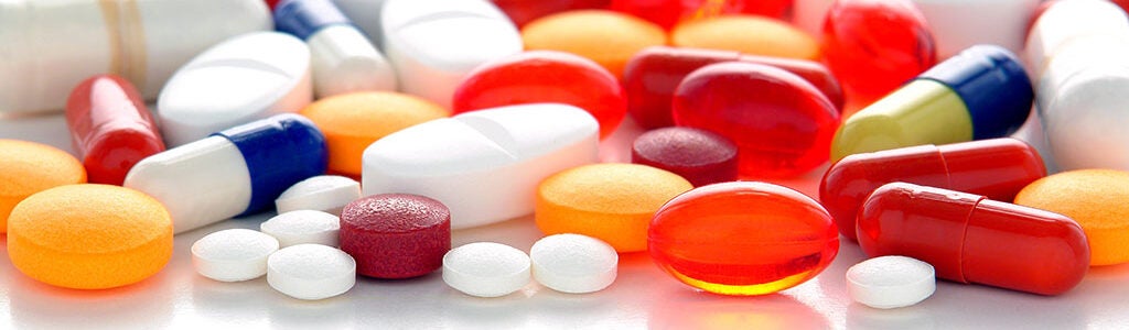 A variety of colorful pills and capsules, including red, white, orange, and yellow ones, scattered on a white surface, representing medication or supplements.