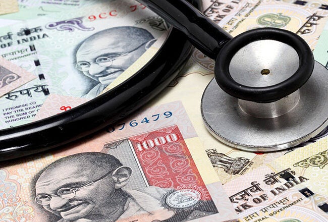 A stethoscope lying on a pile of Indian rupee banknotes, representing the intersection of healthcare and finance.