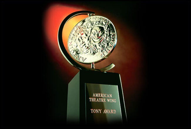 A Tony Award trophy, featuring a metallic medallion with a theatrical design mounted on a black base with "American Theatre Wing" and "Tony Award" inscribed.