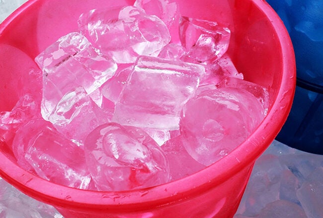 Pink and blue buckets filled with ice cubes on a pile of more ice cubes.
