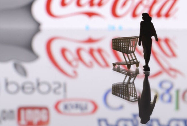 Silhouette of a person pushing a shopping cart with logos of various famous brands in the background, representing consumerism.