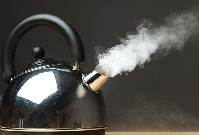 A black kettle with steam coming out of the spout against a dark background.