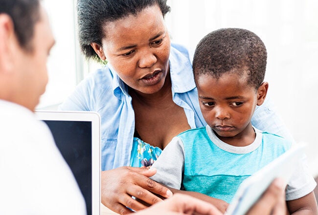 An adult and a child are with another person, looking at a digital tablet. They appear to be in a consultation or instructional setting.