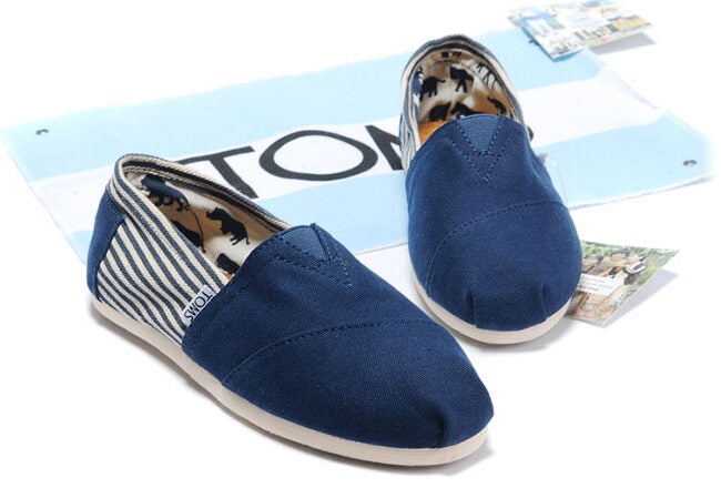 A pair of blue canvas slip-on shoes with a striped lining, displayed on a light blue and white cloth with text partially visible.