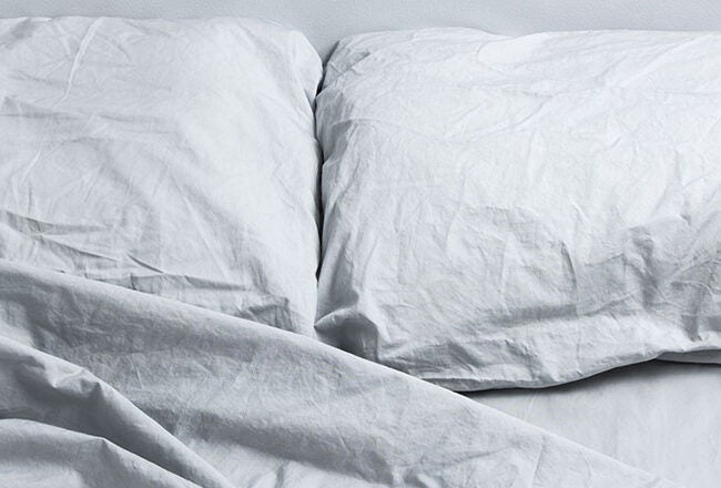Two wrinkled white pillows and a bed with crumpled white sheets, suggesting a recently used or unmade bed.