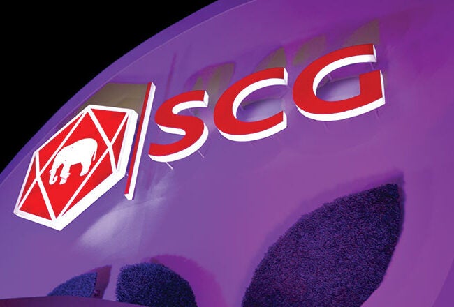 A building facade with the SCG logo, featuring an elephant within a red hexagon and the letters "SCG" in bold red beside it, illuminated against a purple background.