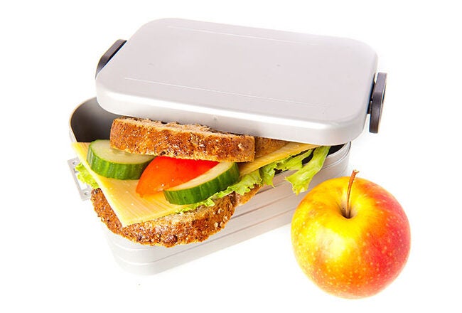 A lunchbox with a sandwich containing lettuce, cheese, cucumber, and tomato, next to a whole apple.