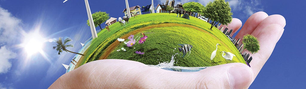 A hand holding a miniature world featuring wind turbines, trees, animals, and houses, symbolizing sustainability and environmental conservation.