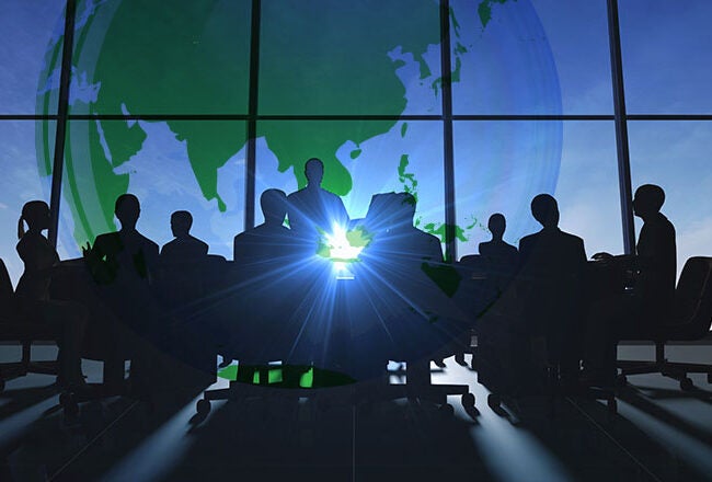 Silhouettes of people sitting around a conference table with a large globe in the background, symbolizing global collaboration.