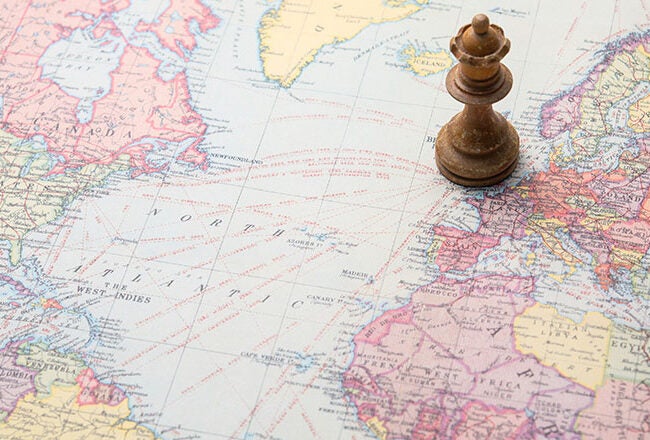 A chess piece, a queen, on a world map positioned over Europe and Africa, symbolizing strategic thinking or global strategy.