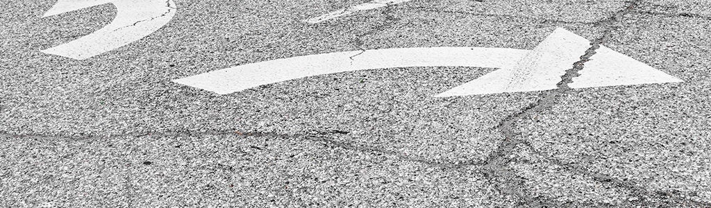 White directional arrows on asphalt, indicating left and right turns, likely on a road surface.