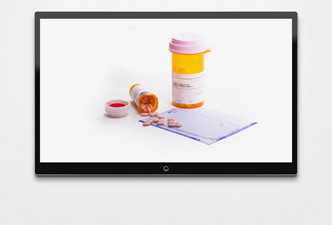 A prescription bottle with pills spilling out, a measuring cup, and a prescription sheet, all displayed on a screen.