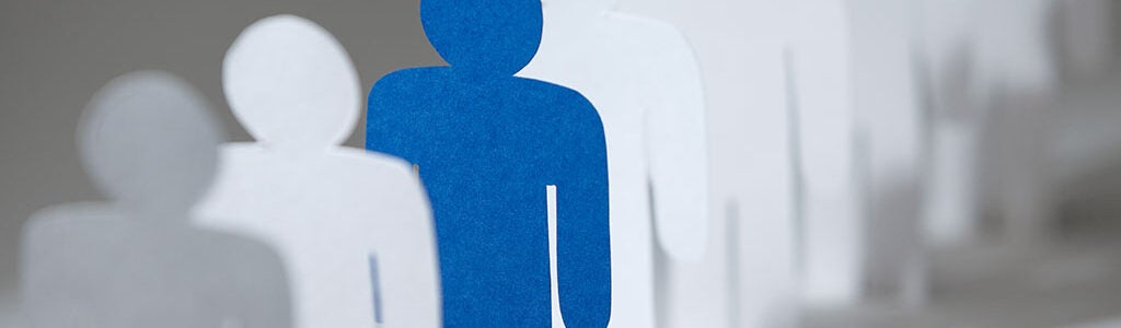 A row of white paper cutout figures with one blue figure standing out in the center, symbolizing individuality or diversity.
