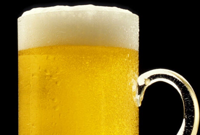 A glass mug filled with golden beer, topped with a layer of frothy foam, against a black background.