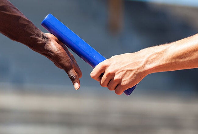 Two people exchanging a blue relay baton during a race, symbolizing teamwork and cooperation.