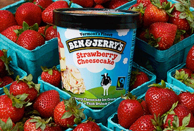 A container of Ben & Jerry''s Strawberry Cheesecake ice cream is surrounded by multiple baskets of fresh strawberries.