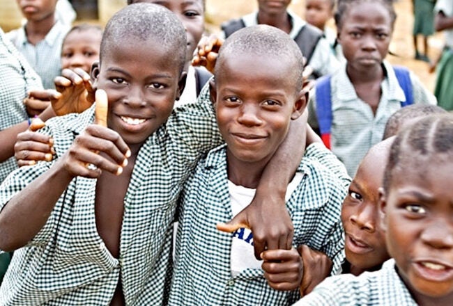 A group of smiling schoolchildren in uniform, gathered closely together outdoors. They appear happy and engaged, suggesting a sense of community and friendship.