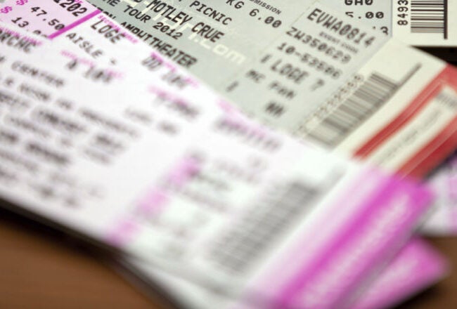 A pile of event tickets, including concert and live event tickets, arranged on a wooden surface.