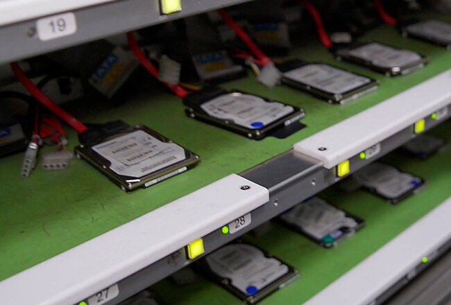 Rows of hard drives on shelves with cables attached, likely representing data storage or a computer server setup.