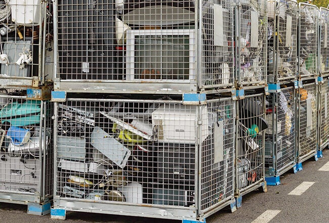 Cages filled with old electronics and appliances, such as monitors and microwaves, stacked in a recycling collection area.