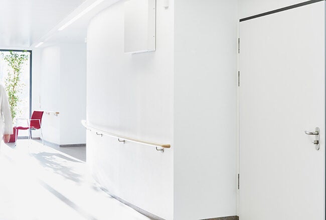 A healthcare professional in a white coat walking down a bright, clean hospital corridor.