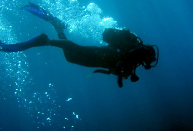 A scuba diver underwater, surrounded by air bubbles, swimming in a deep blue ocean.