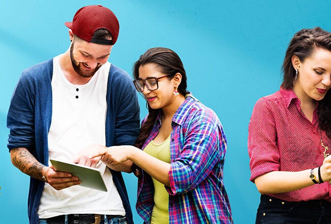 A group of five people standing against a blue background, each engaged with different electronic devices like smartphones and tablets.