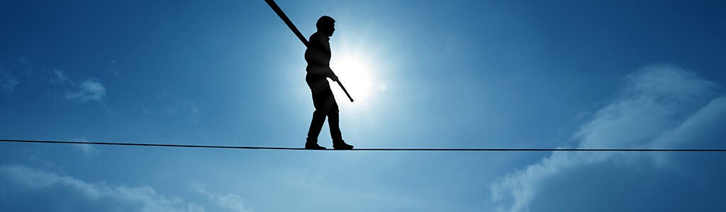 A silhouette of a person walking on a tightrope against a bright sky, holding a balancing pole, symbolizing balance and courage.