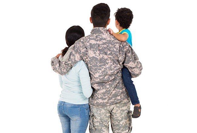 A family seen from behind, with a person in military uniform holding a child and standing next to another adult. This represents family unity and military life.
