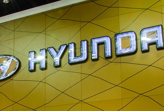 The image shows the Hyundai logo and brand name on a yellow geometric background.