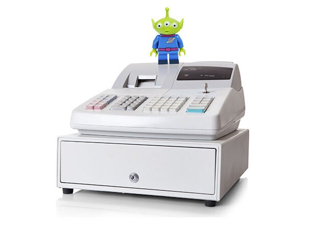 A cash register with a small green alien toy standing on top of it.